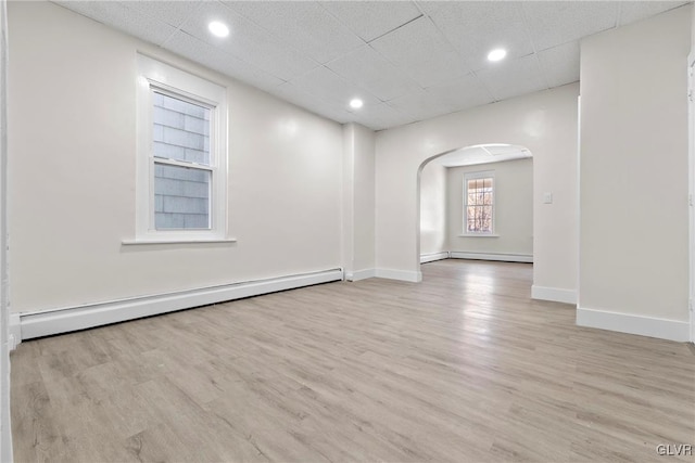 unfurnished room with a drop ceiling, arched walkways, light wood finished floors, baseboards, and baseboard heating