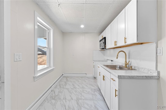 kitchen with stainless steel microwave, light countertops, marble finish floor, white cabinetry, and a sink