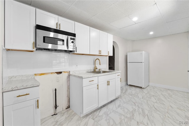 kitchen with arched walkways, freestanding refrigerator, a sink, white cabinets, and stainless steel microwave