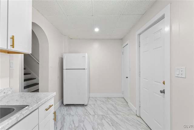 kitchen featuring marble finish floor, white cabinetry, freestanding refrigerator, and baseboards