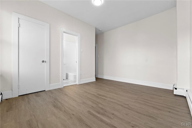 unfurnished bedroom featuring wood finished floors, baseboards, and baseboard heating