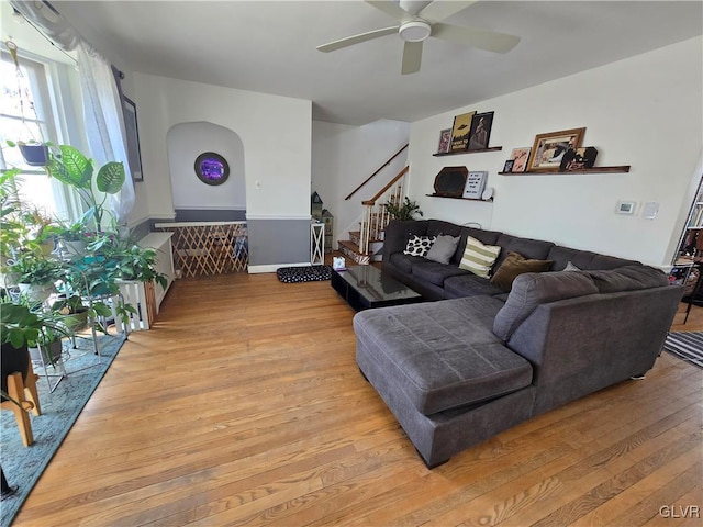 living area featuring light wood-type flooring, stairway, arched walkways, and a ceiling fan