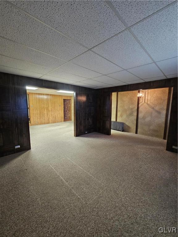 finished below grade area with a paneled ceiling, wood walls, and carpet floors