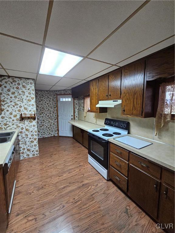 kitchen with wallpapered walls, under cabinet range hood, light countertops, range with electric stovetop, and wood finished floors