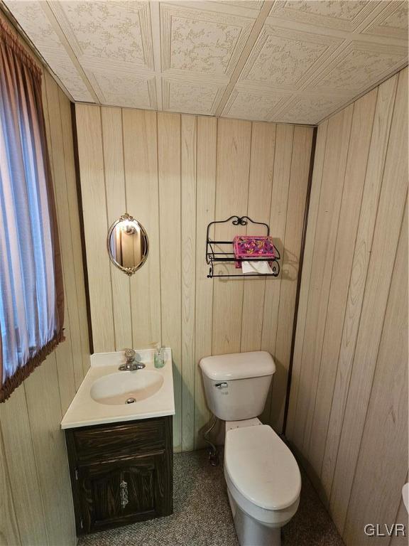 bathroom with vanity, wooden walls, and toilet