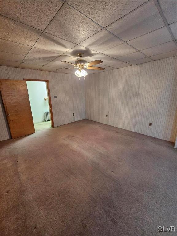 spare room featuring a drop ceiling, light carpet, a ceiling fan, and radiator heating unit