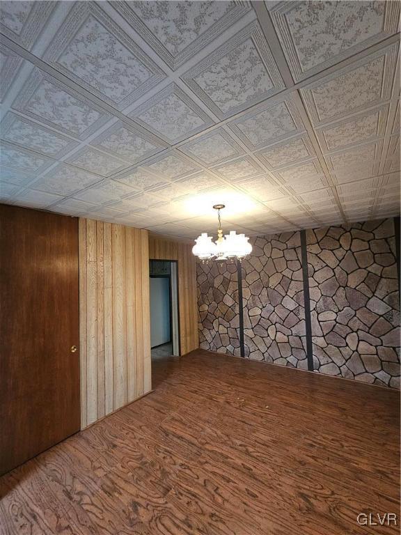 spare room with an ornate ceiling, an inviting chandelier, and wood finished floors