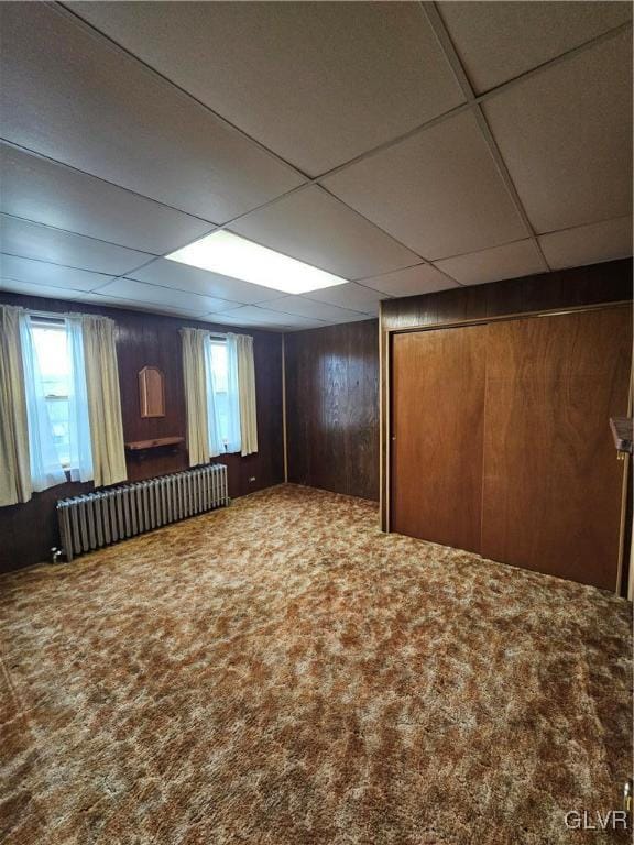 interior space with wood walls, radiator, a paneled ceiling, and carpet floors