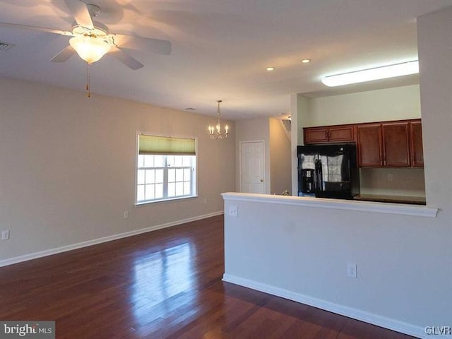 kitchen with dark wood-type flooring, black fridge, ceiling fan with notable chandelier, a peninsula, and baseboards