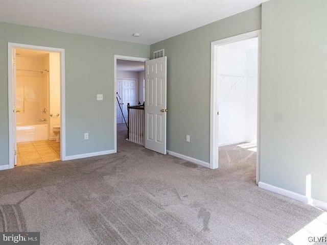 unfurnished bedroom featuring visible vents, connected bathroom, a walk in closet, baseboards, and carpet