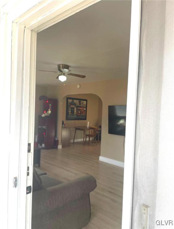 living room featuring baseboards, wood finished floors, arched walkways, and ceiling fan