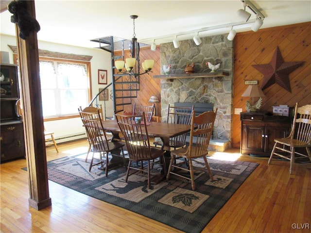 dining space with a baseboard radiator, wooden walls, an inviting chandelier, and hardwood / wood-style flooring