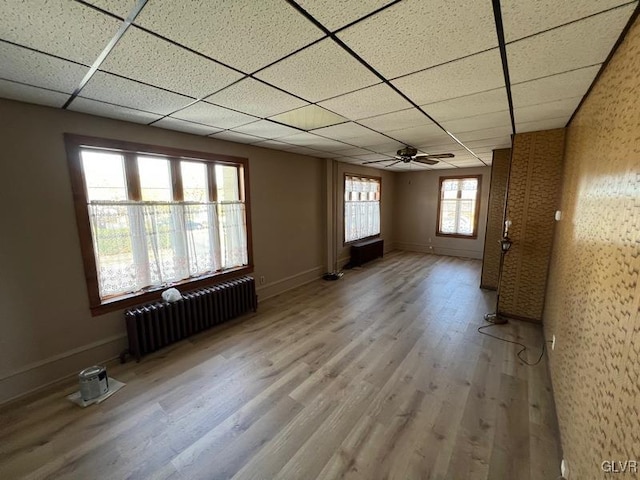 spare room with radiator, a ceiling fan, wood finished floors, baseboards, and a paneled ceiling
