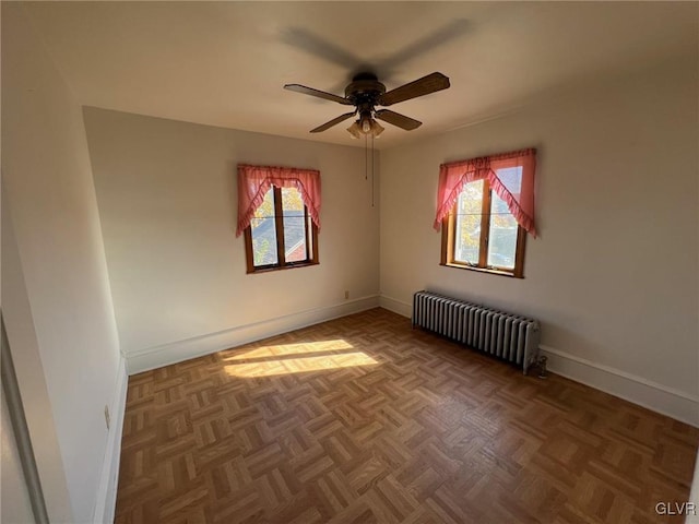 empty room with radiator heating unit, a ceiling fan, baseboards, and a healthy amount of sunlight