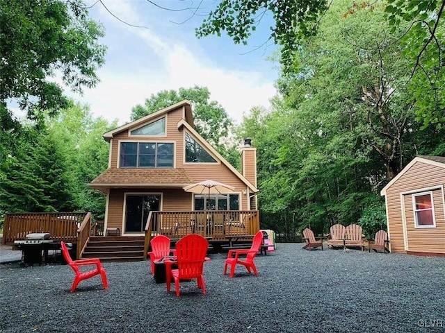 rear view of house featuring roof with shingles, a wooden deck, and a chimney
