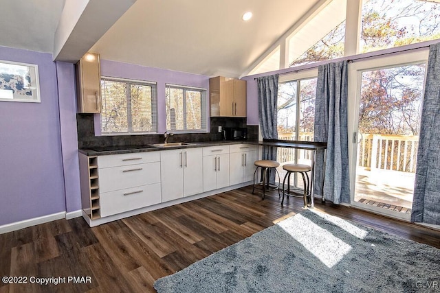 kitchen featuring vaulted ceiling, dark wood finished floors, decorative backsplash, dark countertops, and white cabinets