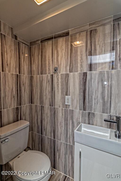 bathroom featuring toilet, vanity, and tile walls
