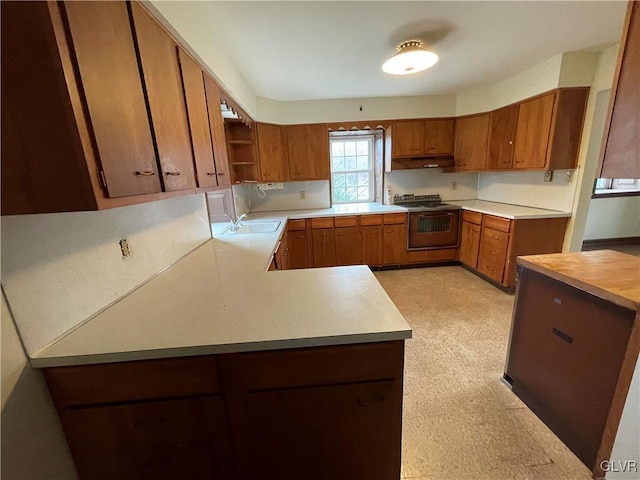 kitchen with under cabinet range hood, range, light countertops, and brown cabinetry
