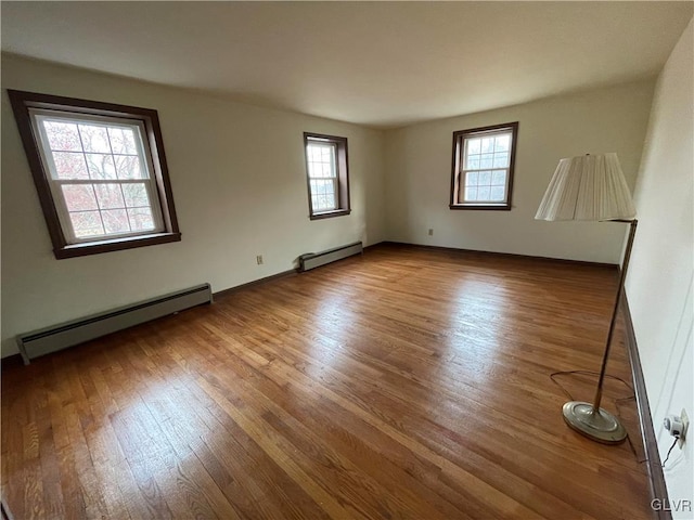 unfurnished room featuring a baseboard radiator, a healthy amount of sunlight, and wood finished floors
