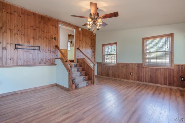 empty room featuring wood walls, stairs, a wainscoted wall, a ceiling fan, and wood finished floors