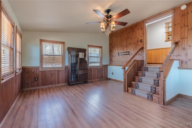unfurnished living room with a wainscoted wall, wood finished floors, stairway, and wooden walls