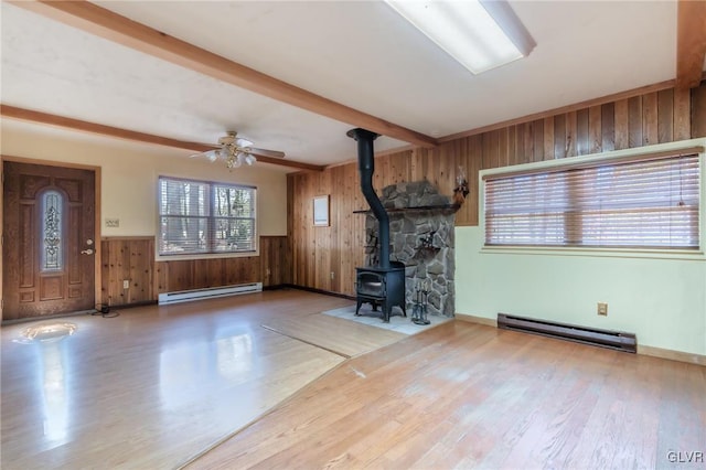unfurnished living room featuring beam ceiling, wood walls, a wood stove, and baseboard heating