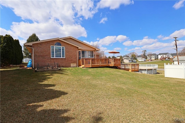 back of property with brick siding, a deck, fence, and a lawn