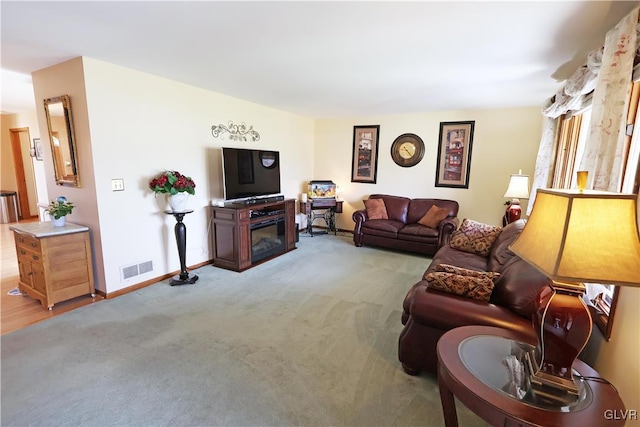 living room featuring visible vents, baseboards, carpet flooring, and a glass covered fireplace