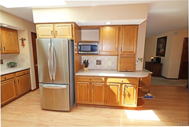 kitchen featuring light countertops, light wood-type flooring, decorative backsplash, and stainless steel appliances
