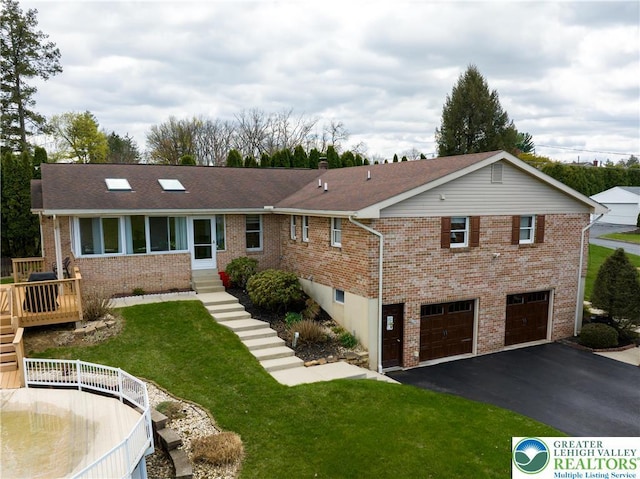 back of property featuring aphalt driveway, a lawn, brick siding, a garage, and a deck
