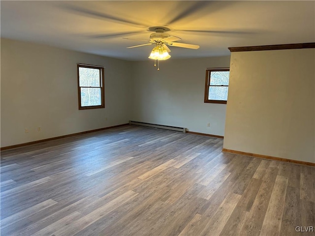 empty room with ceiling fan, a baseboard heating unit, wood finished floors, and baseboards