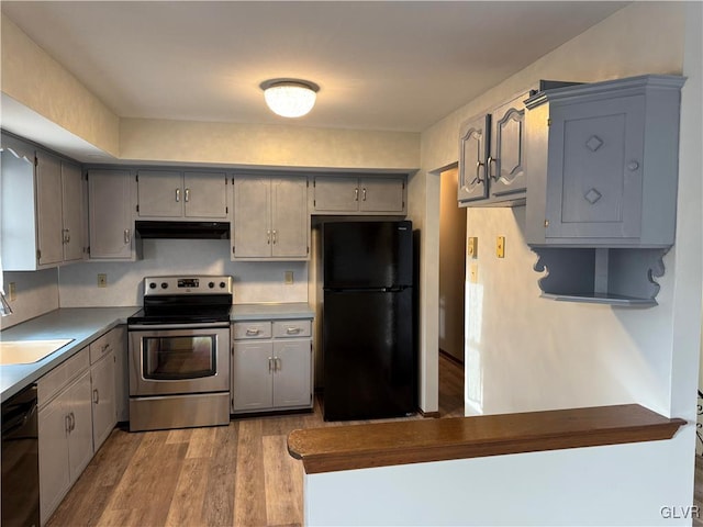kitchen with a sink, light wood-style floors, under cabinet range hood, black appliances, and gray cabinets