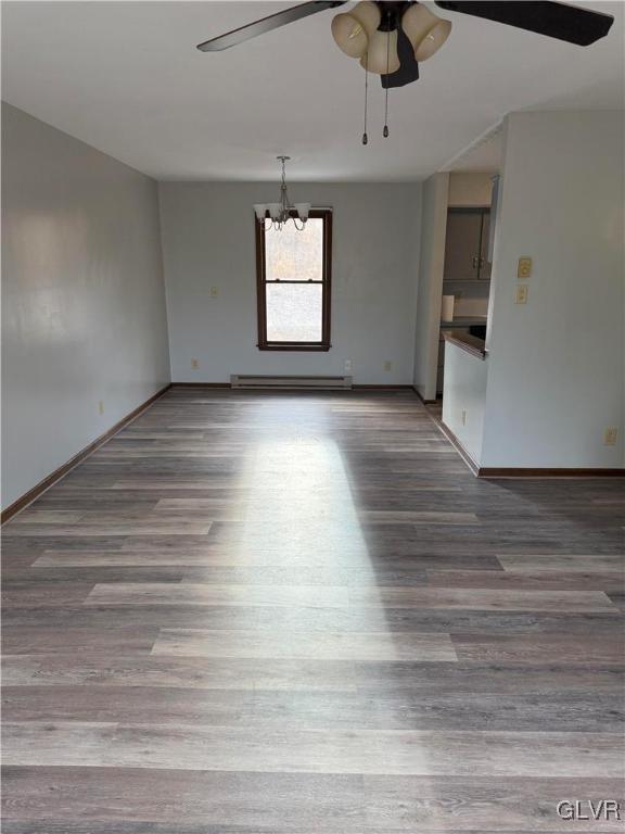 empty room featuring a baseboard heating unit, ceiling fan with notable chandelier, baseboards, and wood finished floors