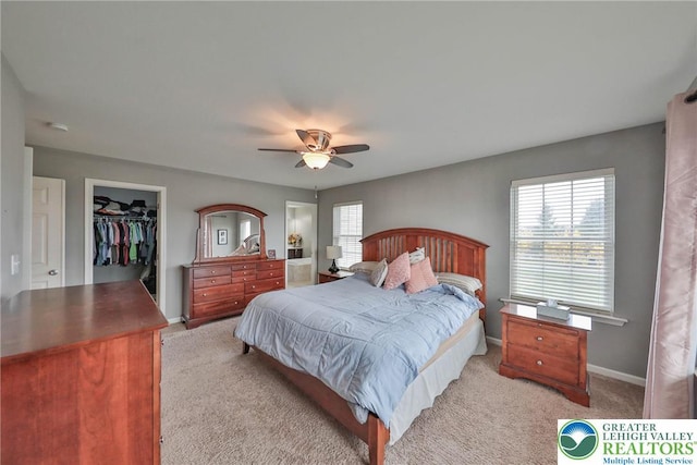 bedroom featuring ceiling fan, a closet, light colored carpet, a walk in closet, and baseboards