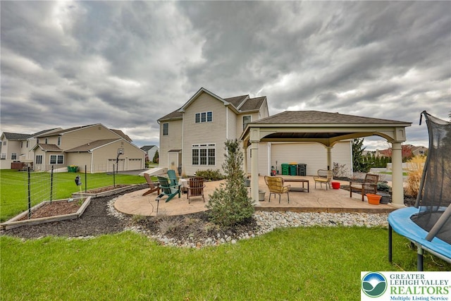 rear view of house with a patio area, an outdoor living space with a fire pit, a gazebo, a trampoline, and a lawn