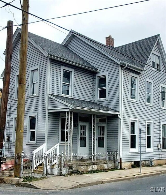 view of front of home with a fenced front yard, roof with shingles, and a chimney