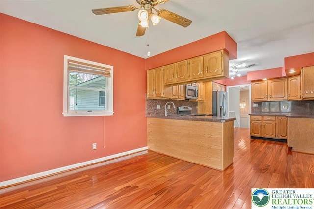 kitchen with a ceiling fan, dark countertops, a peninsula, stainless steel appliances, and light wood-style flooring
