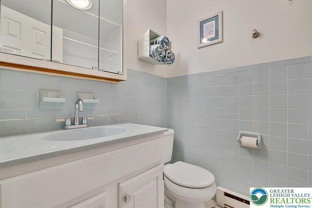 bathroom featuring vanity, baseboard heating, tile walls, and toilet