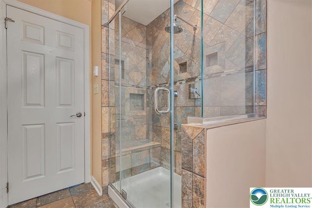 bathroom with a shower stall, stone finish floor, and baseboards