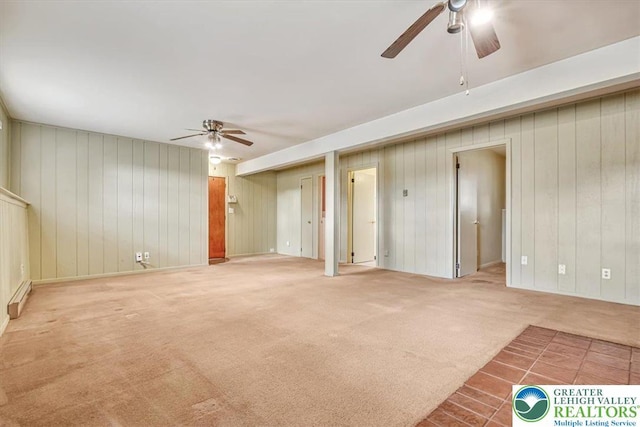 unfurnished living room with wood walls, a baseboard heating unit, ceiling fan, and carpet flooring