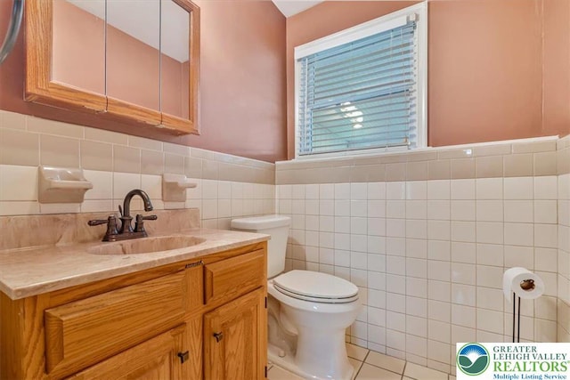 bathroom featuring toilet, vanity, wainscoting, and tile walls