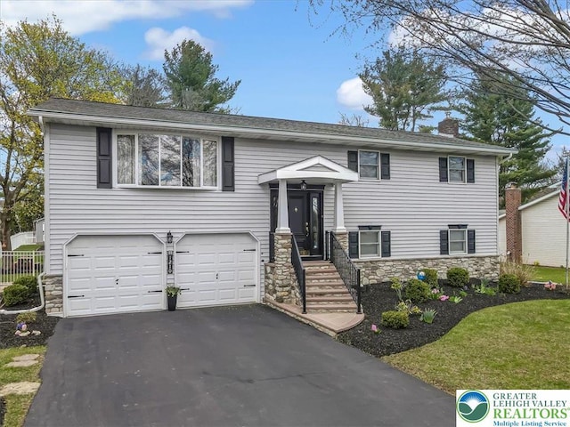 raised ranch with an attached garage, stone siding, a chimney, fence, and driveway