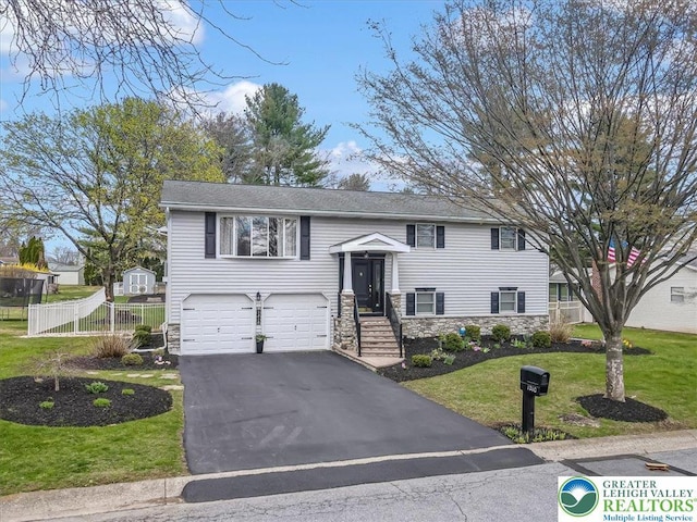 split foyer home with a front yard, stone siding, a garage, aphalt driveway, and fence