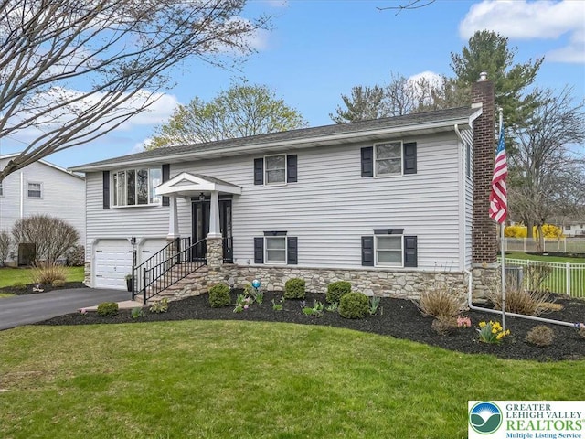 raised ranch with a front yard, an attached garage, a chimney, fence, and driveway