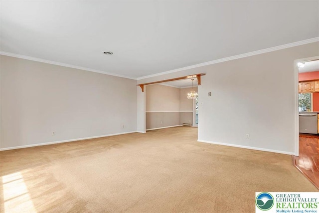 carpeted empty room with a notable chandelier, baseboards, and crown molding