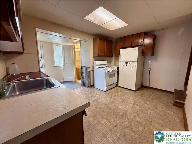 kitchen with a sink, a paneled ceiling, white appliances, and baseboards