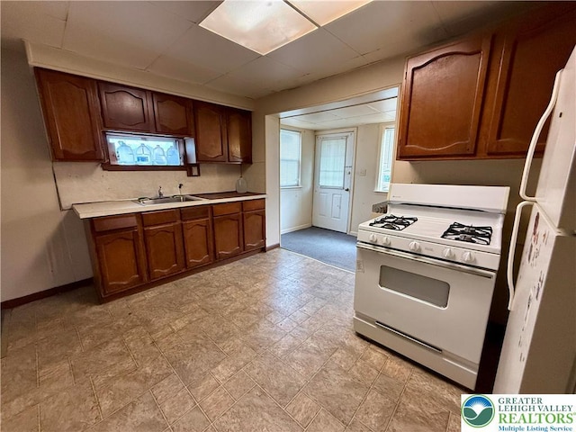 kitchen featuring baseboards, white appliances, light countertops, brown cabinets, and a sink