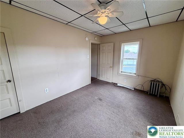 carpeted empty room with ceiling fan, a paneled ceiling, and radiator