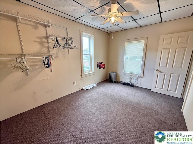 spare room featuring a drop ceiling, radiator, carpet flooring, and a ceiling fan