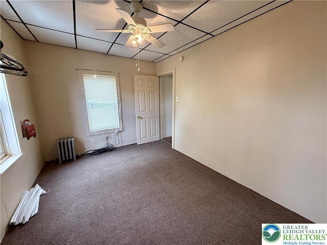 unfurnished room with dark colored carpet, a paneled ceiling, a ceiling fan, and radiator